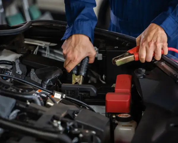 Mekaniker kopplar startkablar till bilbatteriet. Frågan "hur lång tid tar det att ladda ett bilbatteri" är relevant här.