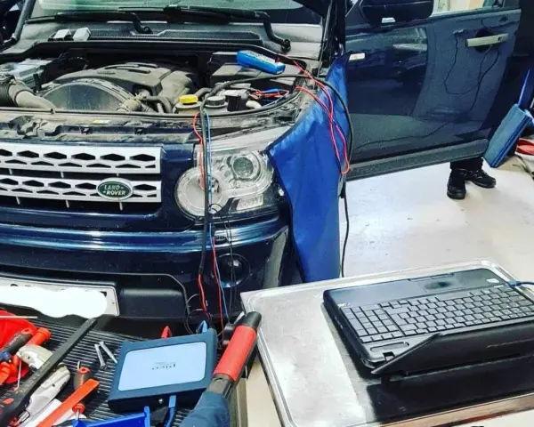 Diagnostik av Land Rover med öppen motorhuv. Kablar kopplade till motor och en dator för felsökning av jordfel bil symtom.