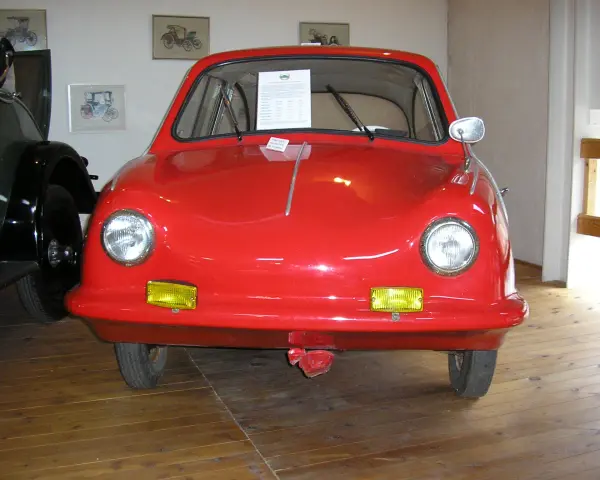 En röd, rundad bil, en Messerschmitt KR200, står på ett trägolv. Fram king Fulda.