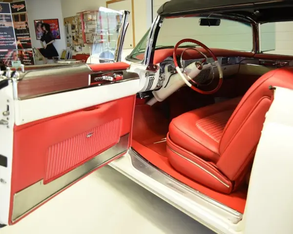En vit cabriolet Cadillac från 50-talet med lyxig röd interiör. Dörren är öppen och visar upp säten och instrumentbräda.