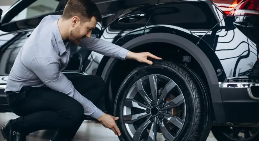 Man inspekterar däcket på en svart bil, redo för ett kumho ecsta ps71 test.