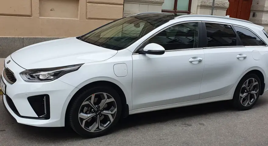 Vit Kia Ceed SW Plug-in Hybrid parkerad på gata. En elsparkcykel syns i bakgrunden.