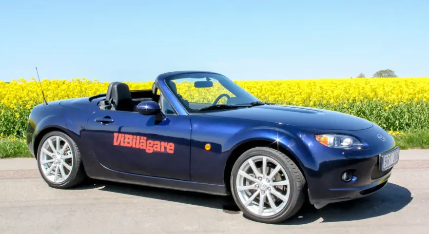 Blå Mazda MX-5 cabriolet parkerad vid en gul rapsåker. Ett potentiellt Mazda MX-5 problem kan vara att den drar till sig uppmärksamhet.