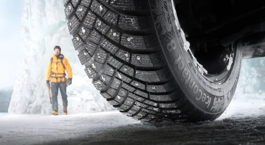 En man i gul jacka står framför en isvägg. Ett Continental IceContact 3-däck med dubb är i förgrunden, redo för test.