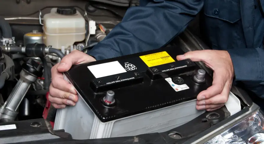 Personen håller i ett bilbatteri för att koppla in det i bilen.