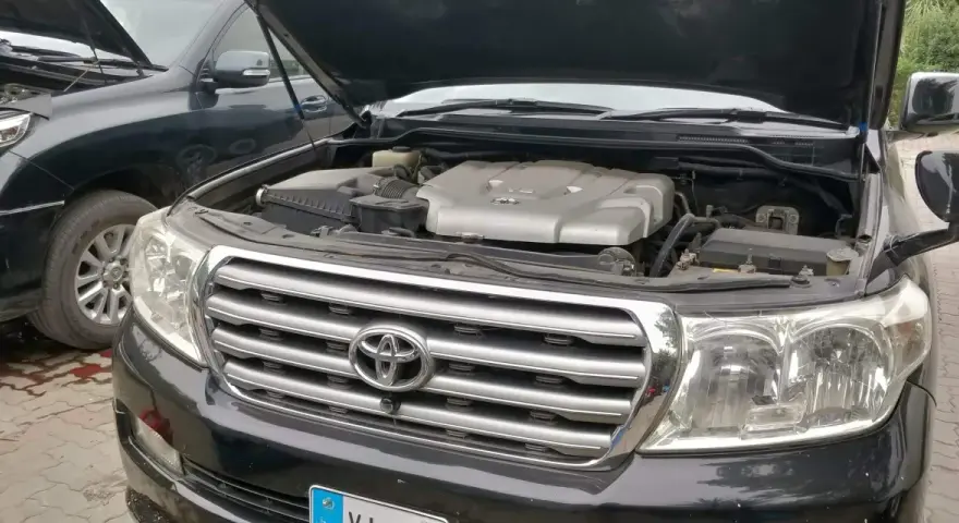 Motorhuven på en svart p0420 Toyota Land Cruiser är öppen, vilket visar V8-motorn. En annan likadan bil står bredvid.