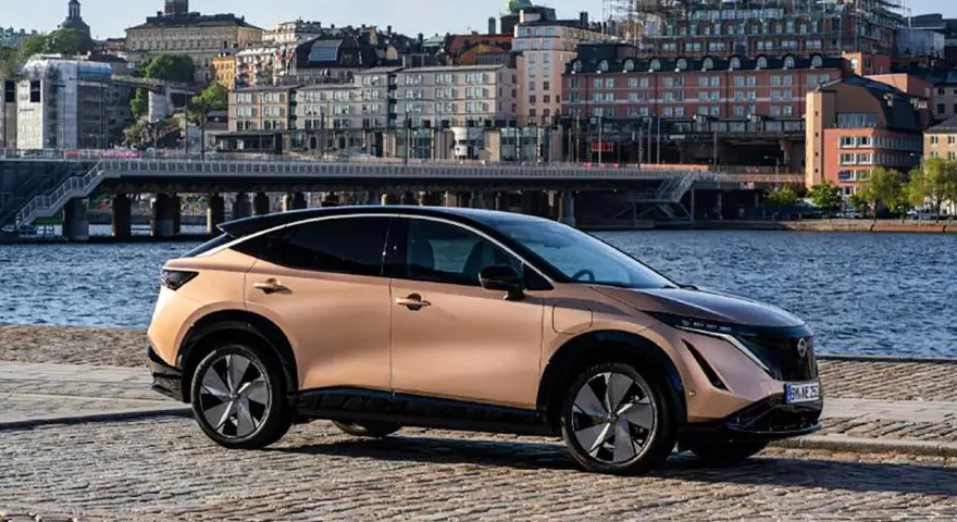 Nissan Ariya testkörning i Stockholm. En elegant elbil parkerad vid vattnet med stadens silhuett i bakgrunden.