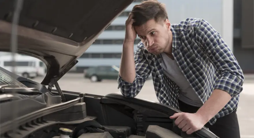 Man med bekymrat ansikte tittar ner i motorhuvens öppning. Han verkar fundera på varför bilen låter konstigt vid tomgång.