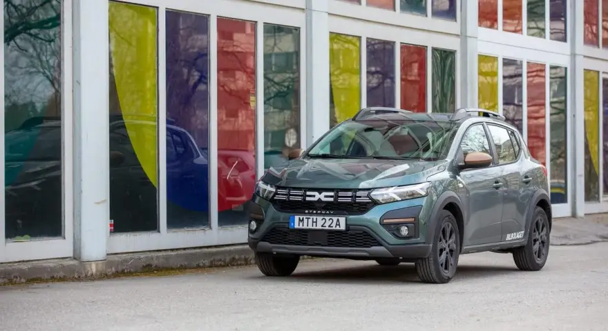 Grön Dacia Sandero Stepway, redo för ett däcktest. Bilen står parkerad framför en byggnad med färgglada fönster.