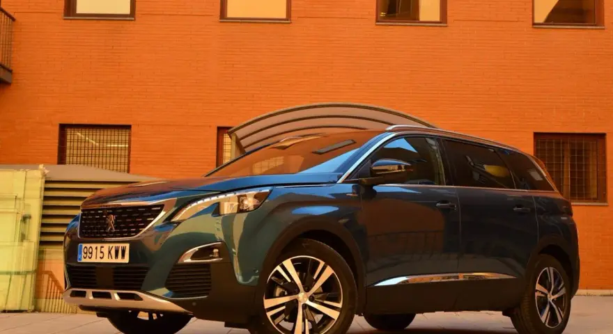 Mörkblå Peugeot 5008 SUV parkerad framför en orange tegelbyggnad. En perfekt bil för en familjeresa, en riktig peugeot 5008 test.