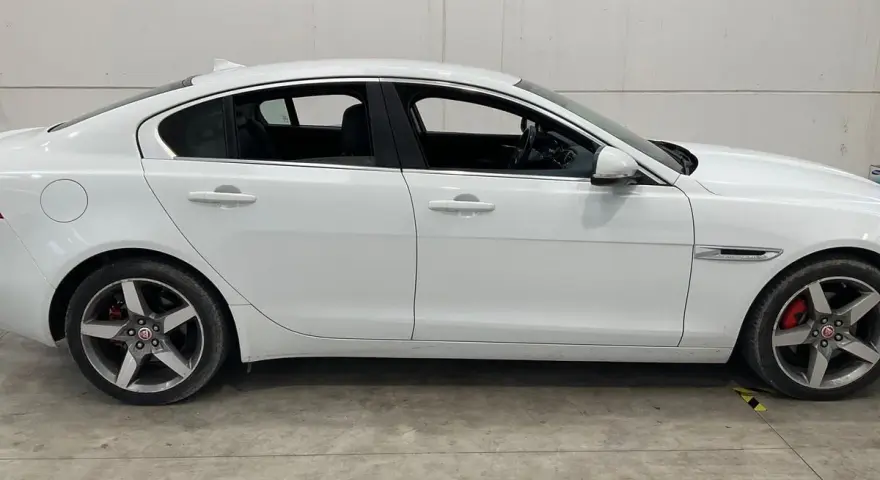 Vit Jaguar XE, sidovy. En bil med ett potentiellt jaguar xe problem, står parkerad på ett betonggolv.