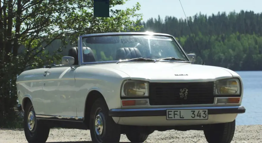Vit cabriolet Peugeot 304 står vid en sjö.
