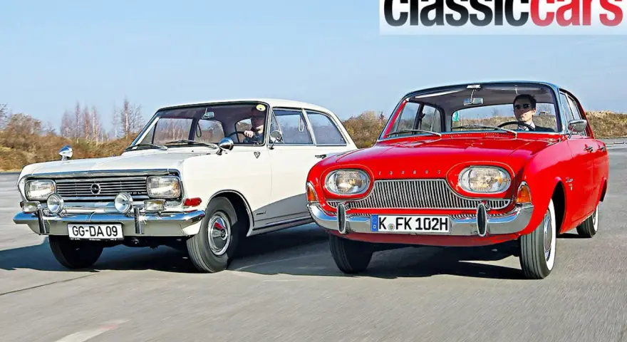 Två klassiska bilar, en vit och en röd, kör på en väg. Den röda bilen är en Ford Taunus från 1960.