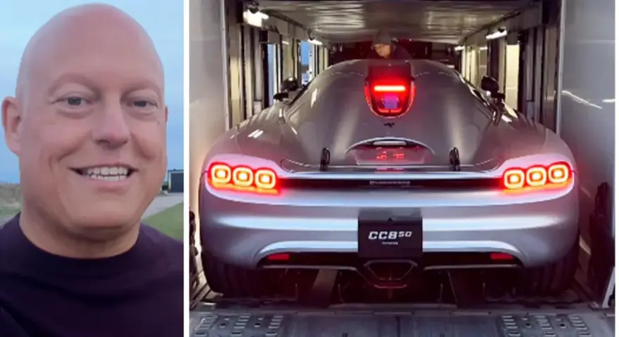 En man ler bredvid en silverfärgad Koenigsegg CC850 som lastas in i en trailer.