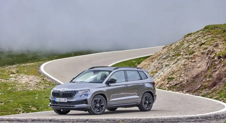 Grå Skoda Karoq på en slingrig bergsväg, omgiven av dimma och grönska. Inga problem här, bara en vacker utsikt.