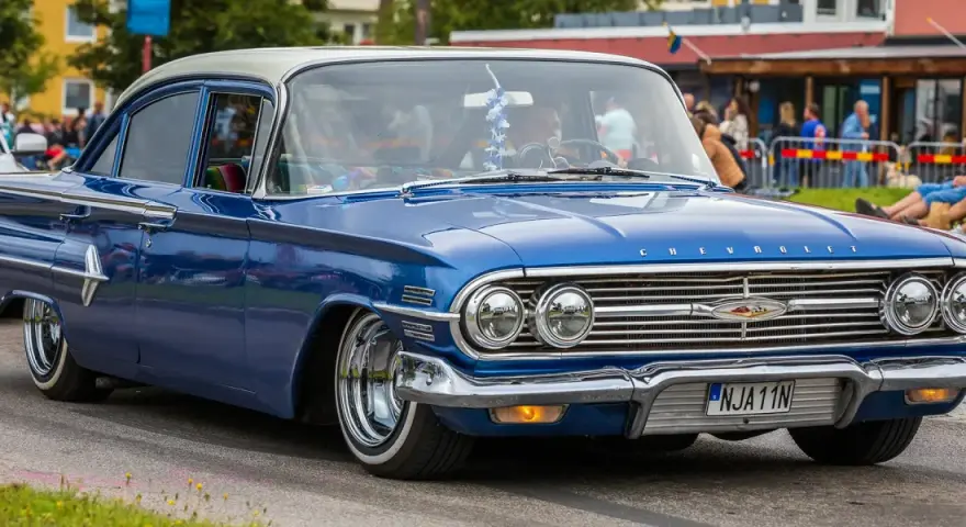 En blå klassisk bil, en Chevrolet, rullar fram på en gata.