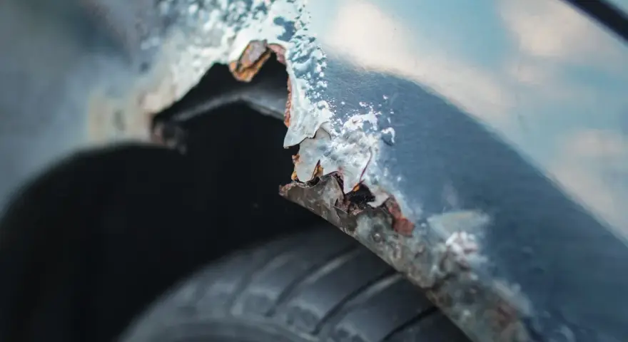 Detaljerad bild av rostskador på en bilskärm, en tydlig indikation på att det är dags att laga rost på bilen. Däcket syns nedtill.