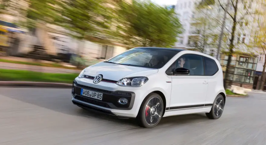 Vit VW Up GTI med svarta detaljer kör genom en stad.