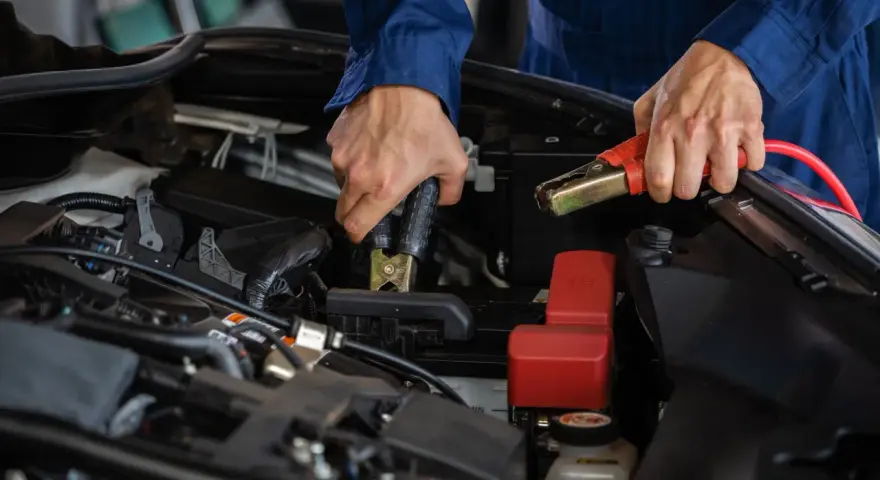 Mekaniker kopplar startkablar till bilbatteriet. Frågan "hur lång tid tar det att ladda ett bilbatteri" är relevant här.