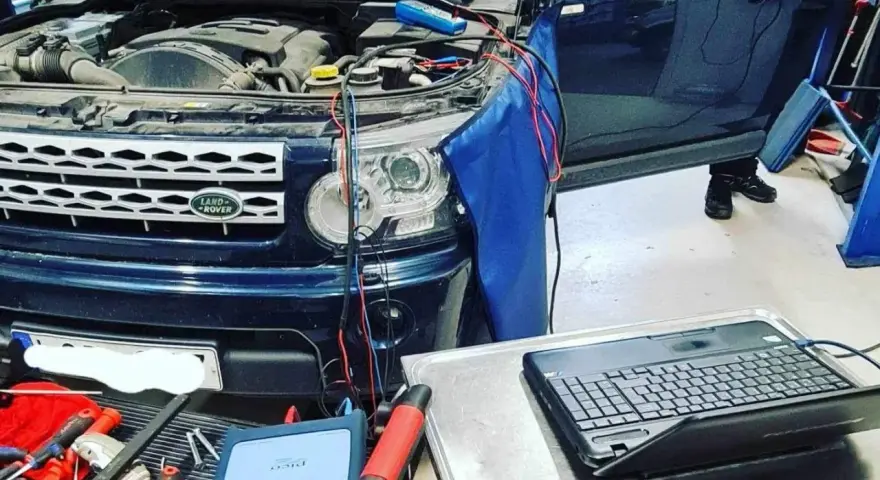 Diagnostik av Land Rover med öppen motorhuv. Kablar kopplade till motor och en dator för felsökning av jordfel bil symtom.
