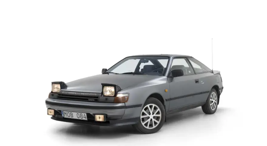 Grå Toyota Celica 1986 med pop-up-strålkastare, redo för en nostalgisk resa.