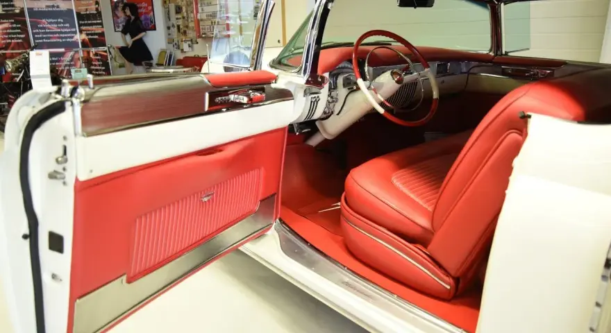 En vit cabriolet Cadillac från 50-talet med lyxig röd interiör. Dörren är öppen och visar upp säten och instrumentbräda.