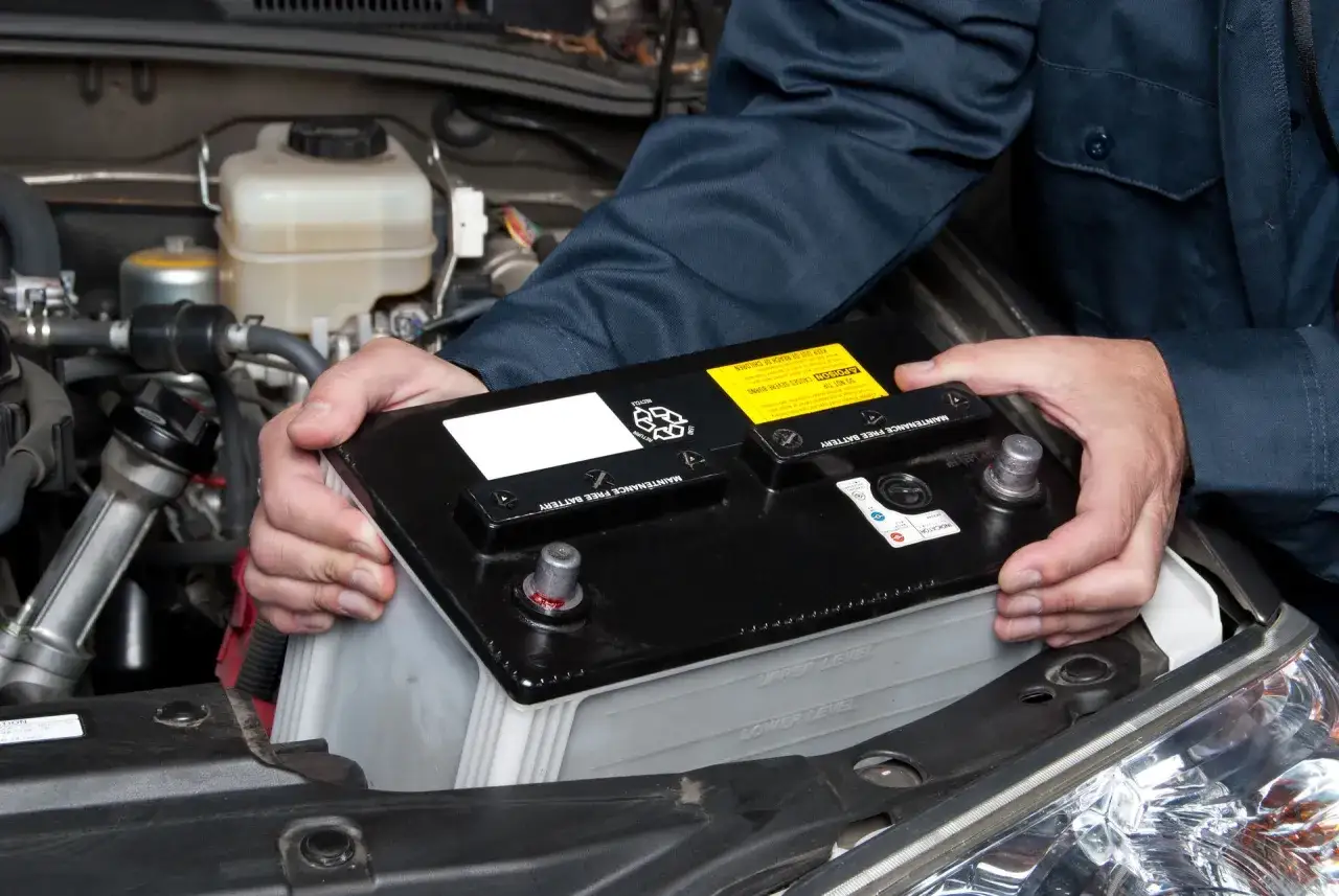 Mekaniker byter ett urladdat bilbatteri i motorutrymmet.