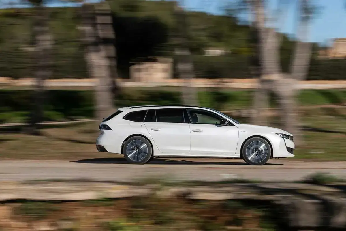 Vit Peugeot 508 SW i fart under ett test. Bilen glider fram l&auml;ngs en v&auml;g med suddig bakgrund av tr&auml;d och stenar.