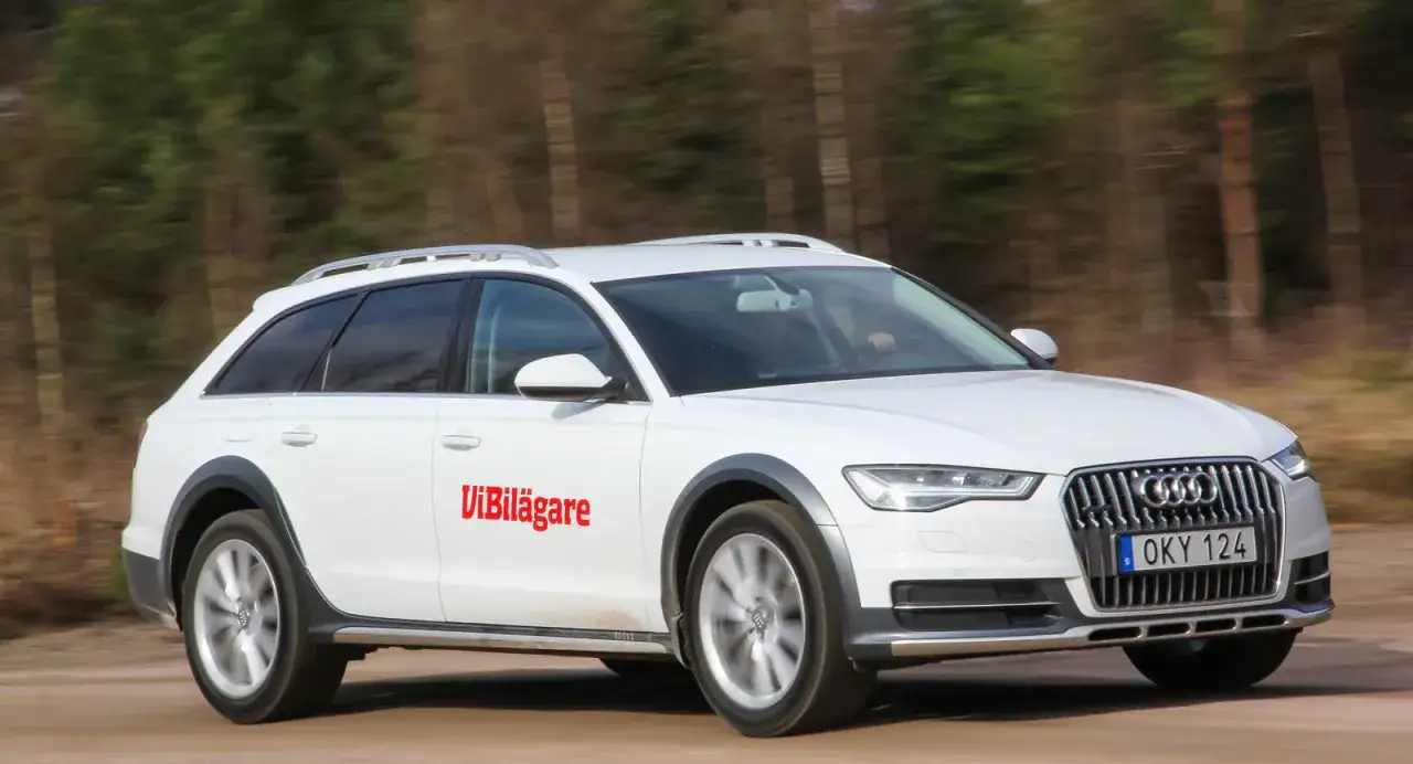 Vit Audi A6 Allroad kör på grusväg, med texten