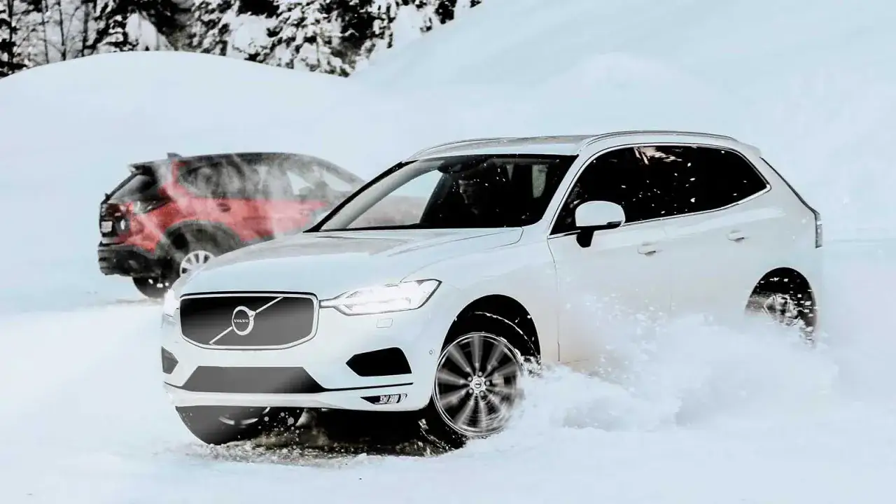 Vit Volvo kör genom snö, en röd bil syns i bakgrunden. Frågan är: fyrhjulsdrift eller inte?