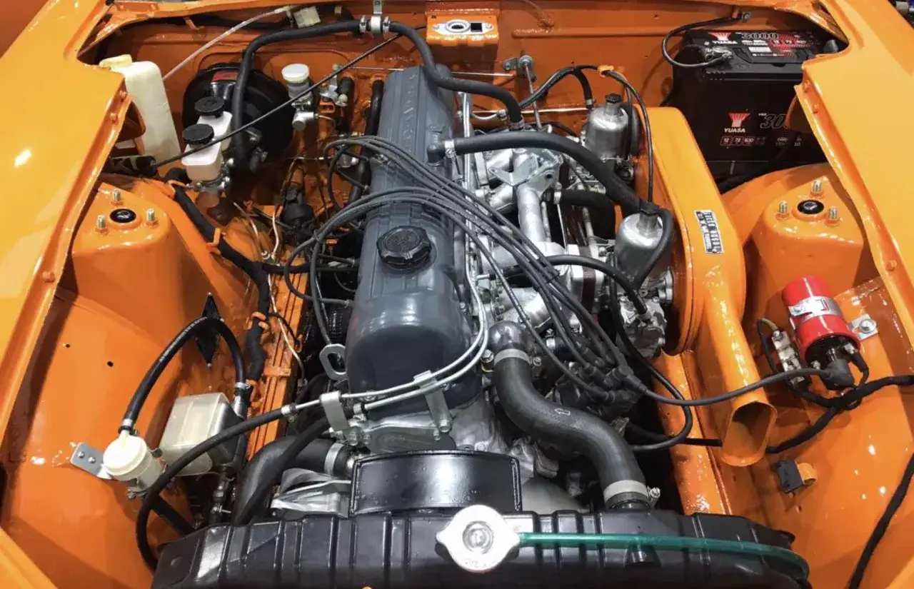 Motorutrymmet i en orange Nissan Datsun 240Z, med fokus på den klassiska motorn och dess komponenter.