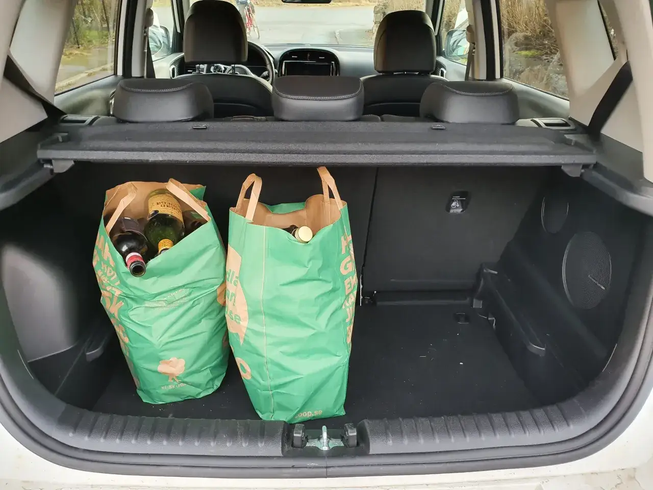 Tv&aring; gr&ouml;na kassar med flaskor st&aring;r i bagageutrymmet p&aring; en Kia Soul. En lyckad matink&ouml;p, redo f&ouml;r hemf&auml;rd.