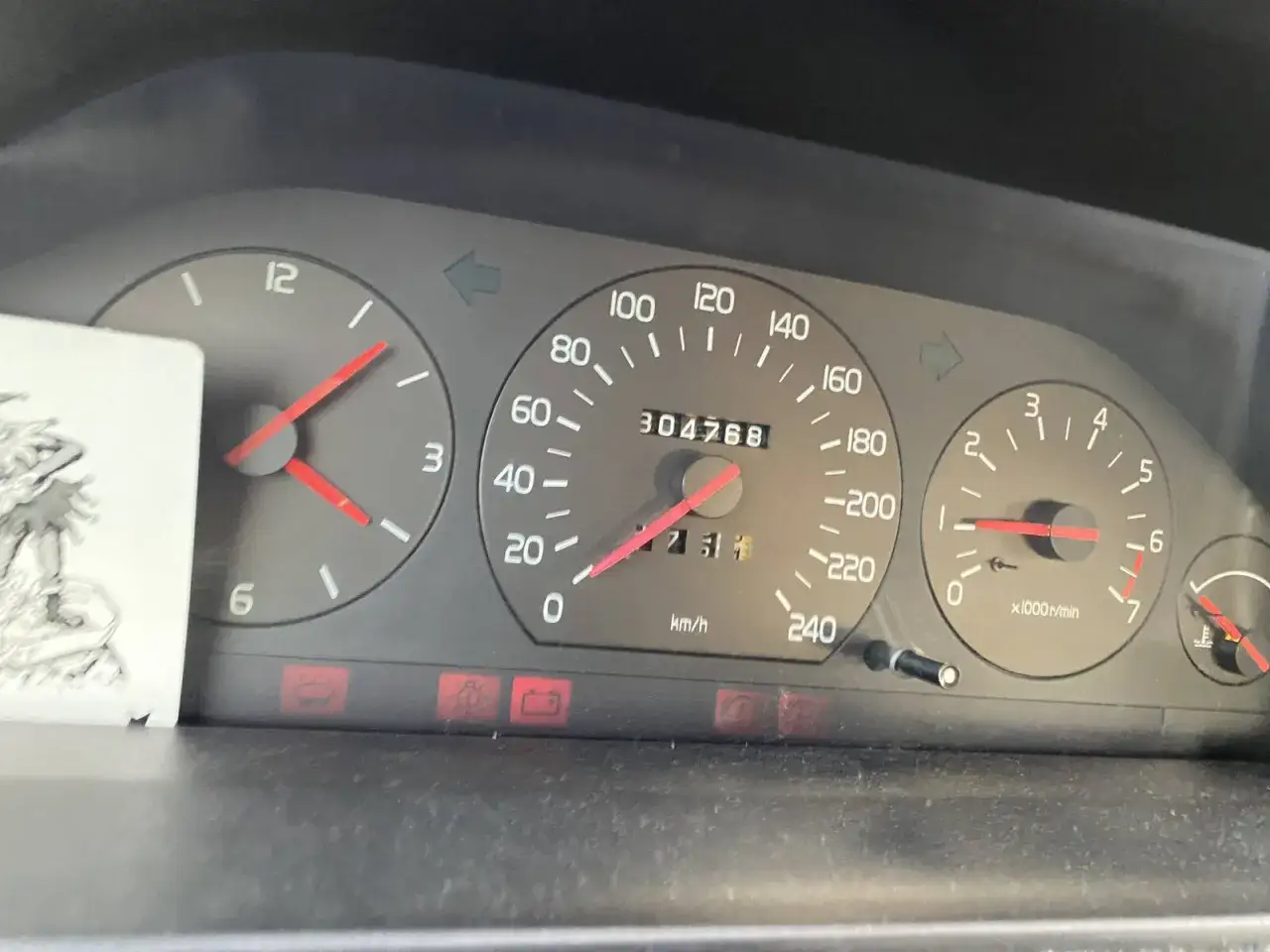 Varningslampor på en Volvo 940-instrumentpanel lyser. Kilometermätaren visar 304768.