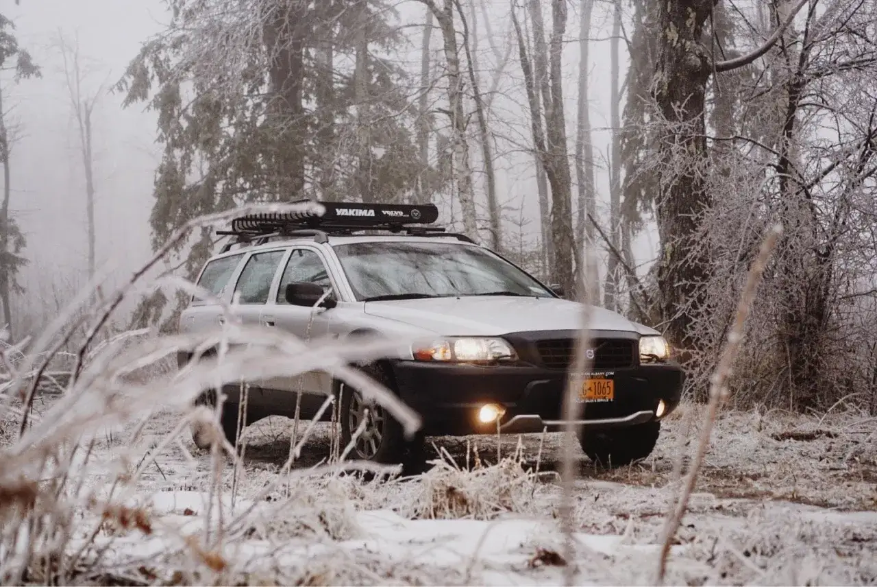 Silver Volvo XC70 med takräcke redo för äventyr i en frostig skog.