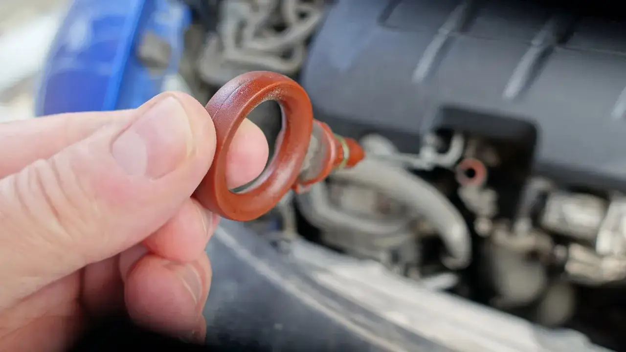 En hand håller i oljestickan för att kolla olja bil. Motorn är synlig i bakgrunden.