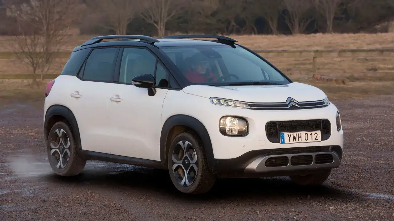 Vit Citroën C3 med svart tak kör på grusväg. En förare syns bakom ratten. Kanske ett litet citroën c3 problem med dammet?