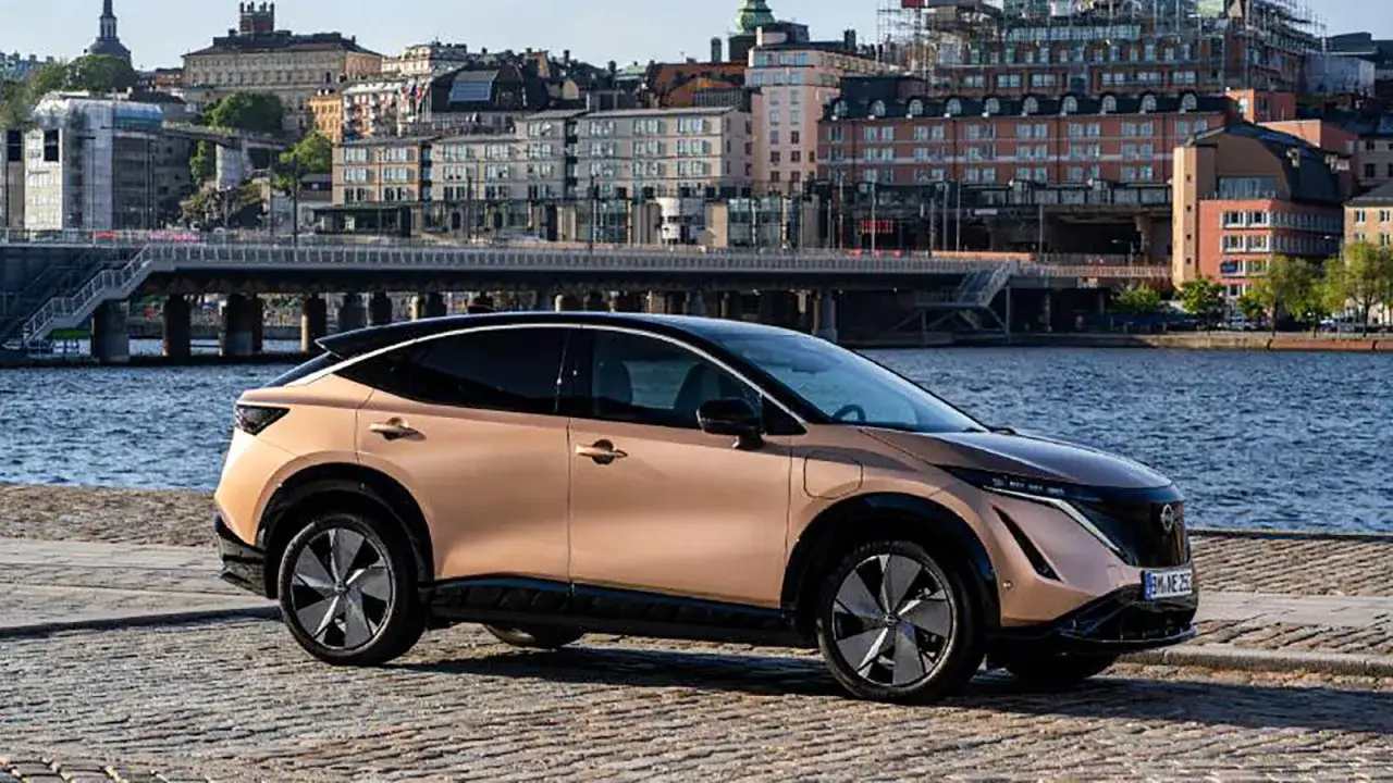 Nissan Ariya testkörning i Stockholm. En elegant elbil parkerad vid vattnet med stadens silhuett i bakgrunden.