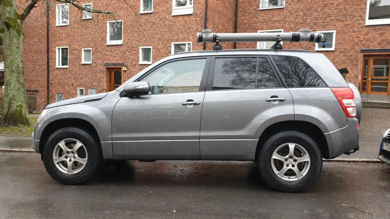 Grå Suzuki Grand Vitara med ett rör på taket, kanske ett problem med transporten.