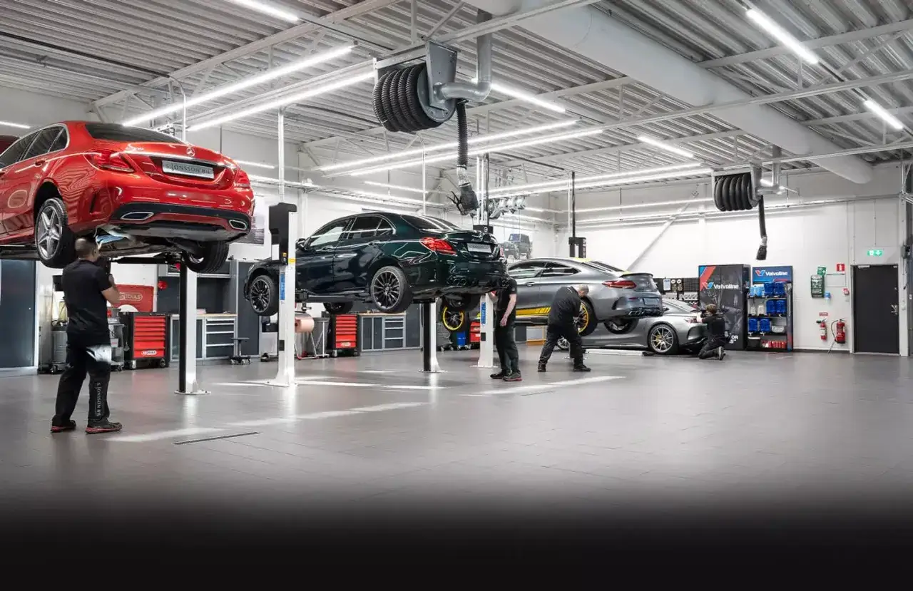 Verkstad med flera Mercedes-bilar på lyftar, redo för service. En röd, en mörkgrön och en silverfärgad bil syns.