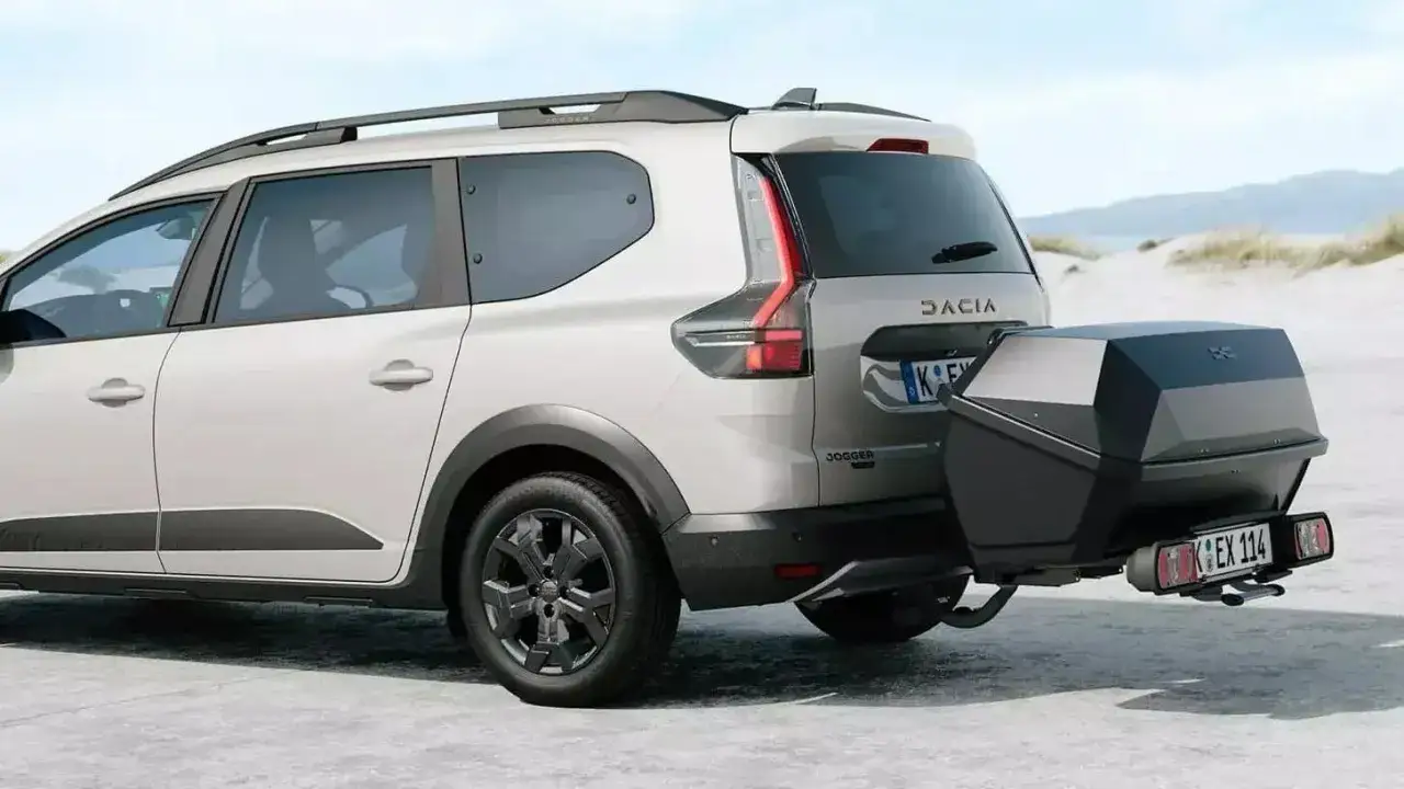 Dacia Jogger test: En vit Dacia Jogger med takr&auml;cke och en svart takbox bak, redo f&ouml;r &auml;ventyr p&aring; en sandig strand.