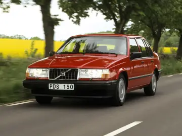 En röd 740 Volvo kör längs en landsväg, med en gul rapsåker och träd i bakgrunden.