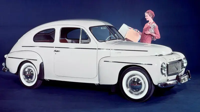En elegant vit Volvo PV 444 med en kvinna och en hund bredvid.