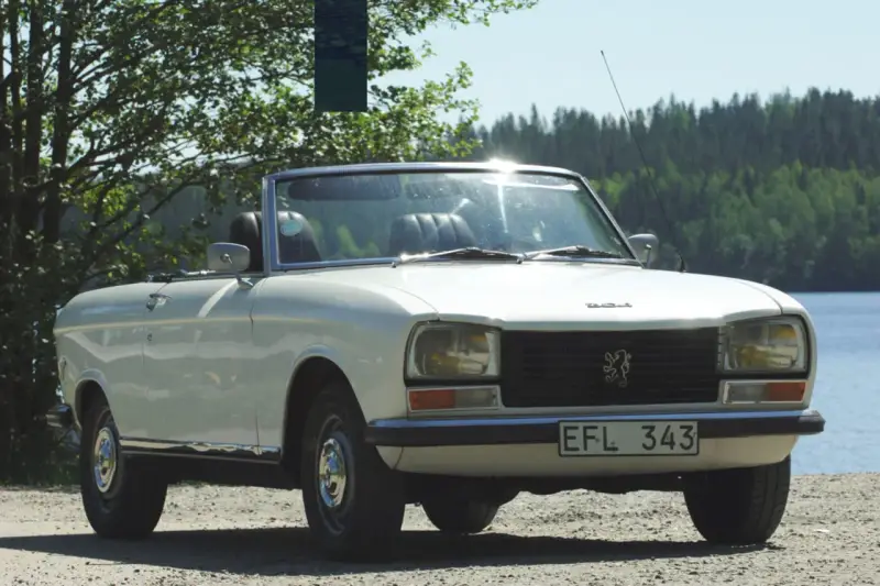 Vit cabriolet Peugeot 304 står vid en sjö.