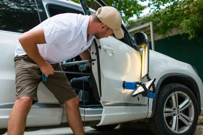 Man fixar en buckla på bilen med specialverktyg och ljus.